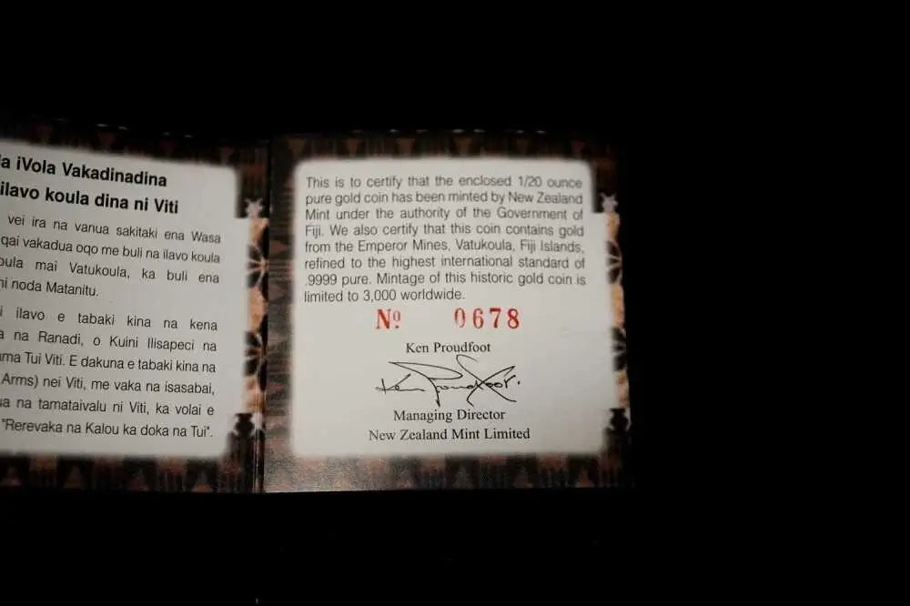 A close-up of a certificate insert for a Fiñ gold coin, showing text and signatures on a dark background.