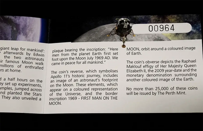 A close-up of a coin or collectible plaque insert with printed text about moon exploration and an astronaut orbit illustration. The visible text includes 'MOON, orbit around a coloured image of Earth.