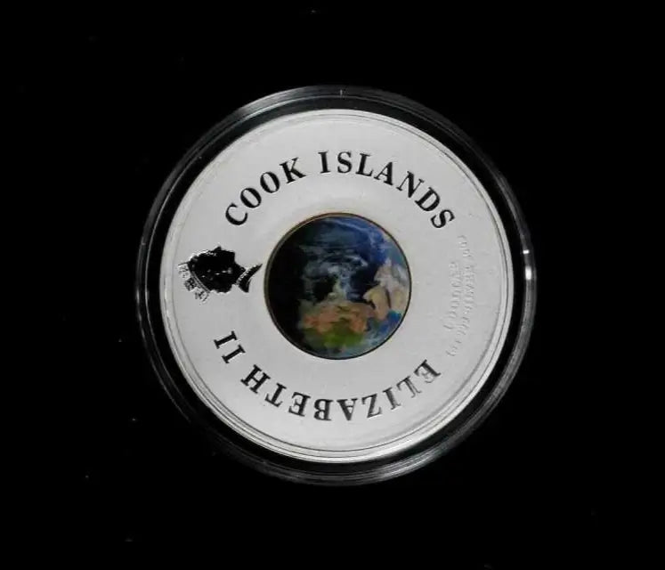 A round silver Cook Islands coin in a clear protective capsule, featuring a central globe design and the text 'COOK ISLANDS' and 'ELIZABETH II' on a black background.