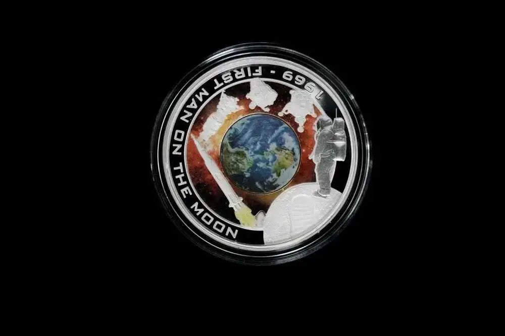 A circular commemorative coin or medallion featuring a silver-toned border with the text '1969 - FIRST MAN ON THE MOON' and 'JEEP 699', surrounding an Earth globe and space-themed illustration, shown on a black background.