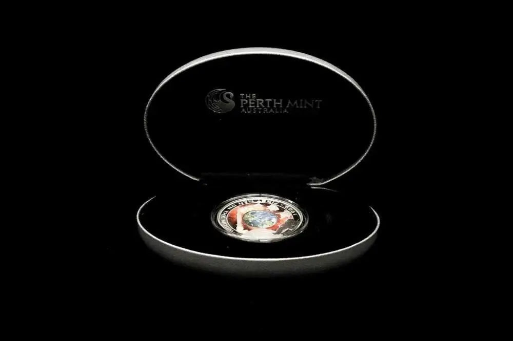 A Perth Mint coin displayed inside an open oval presentation box on a black background. The silver-toned coin is centered in the lower half of the open lid, and the inside lid is printed with the Perth Mint logo and text.