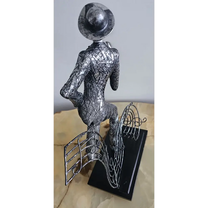 Metallic sculpture of a figure with a hat on a stand against a light background