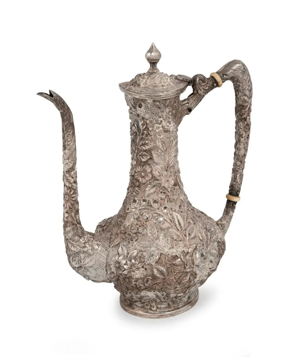 An ornate silver pewter coffee pot with intricate floral engravings, a long curved spout, and a decorative handle, shown on a white background.