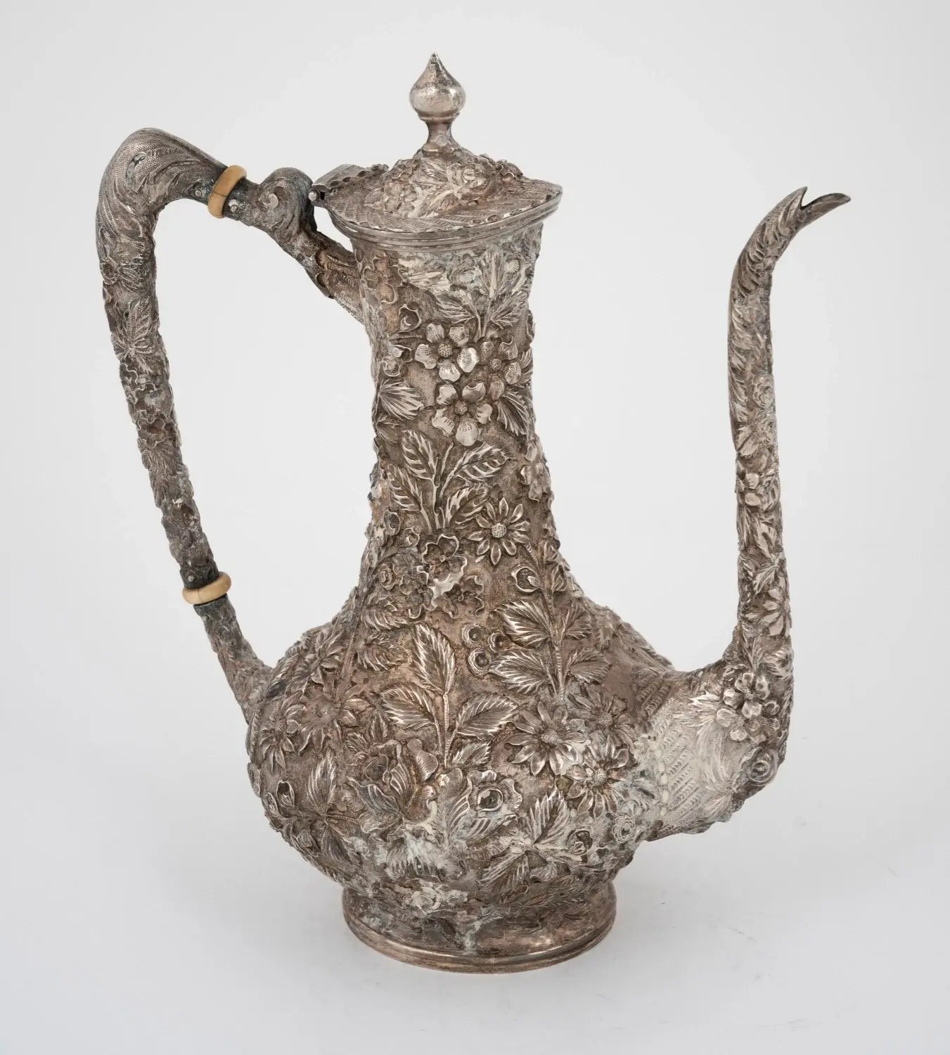 An ornate antique silver teapot decorated with intricate floral engravings, featuring a curved handle, a long spout, and a lid with a finial top, shown against a plain light background from our Antique & Vintage Collectibles Australia collection 