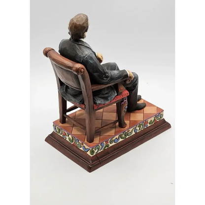 Statue of a person sitting on a chair with a decorative base on a white background