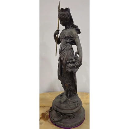 Bronze statue of a woman holding a spear and fruit on a wooden base with a white background