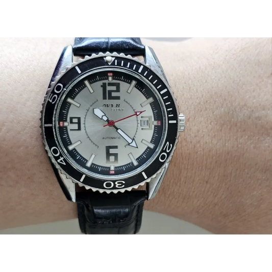 Black wristwatch with a silver bezel on a wrist against a neutral background