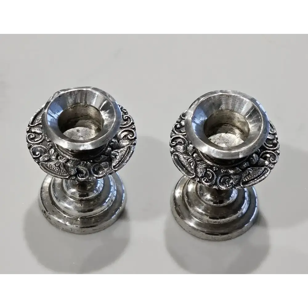 Two silver candle holders with intricate designs on a white background