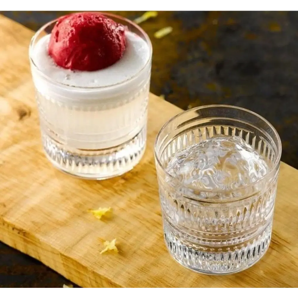 Two glasses on a wooden surface, one with a dessert and the other with a clear liquid.