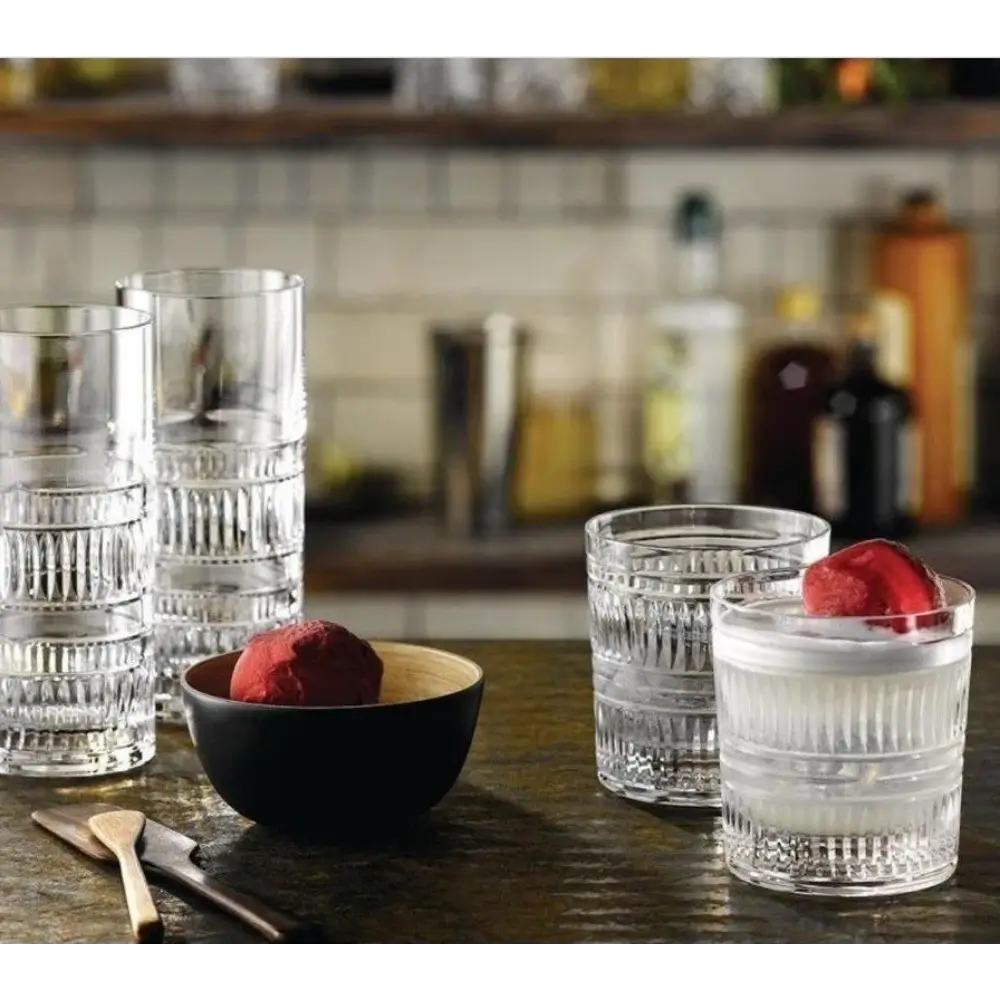 Clear glass tumblers with a bowl of red fruit on a wooden surface.