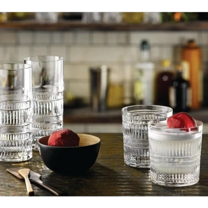 Clear glass tumblers with a bowl of red fruit on a wooden surface.