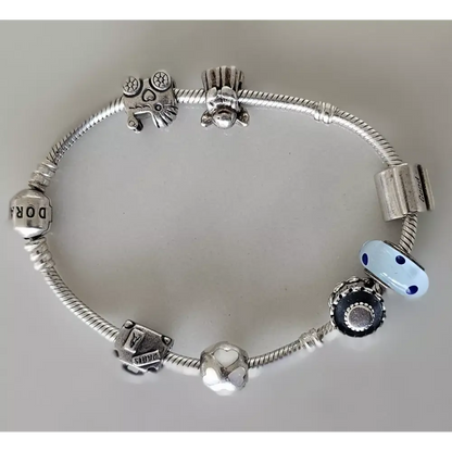 Silver charm bracelet with various charms on a light gray background