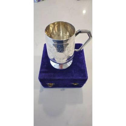 Silver cup with engraved design on a purple cushioned stand