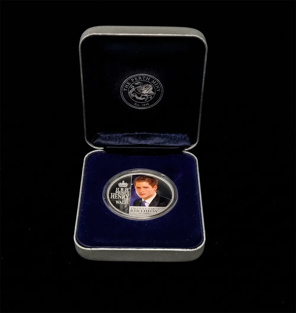 A commemorative silver coin presented in an open dark blue velvet box with a silver border, photographed against a solid black background. The coin features a portrait of John Henry Wilkes and the text 'JOHN HENRY WILKES' and 'MERRY END'.