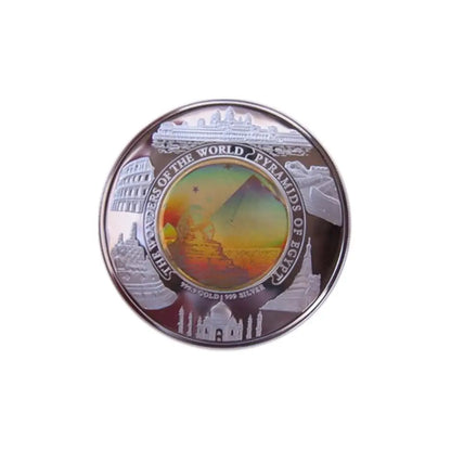 A round commemorative coin featuring the Great Pyramid of Giza at the center, surrounded by silhouettes of other ancient landmarks including the Colosseum, Taj Mahal, and the Eiffel Tower. The outer ring is inscribed with 'SEVEN Wonders of the World - Pyramids of Giza'.