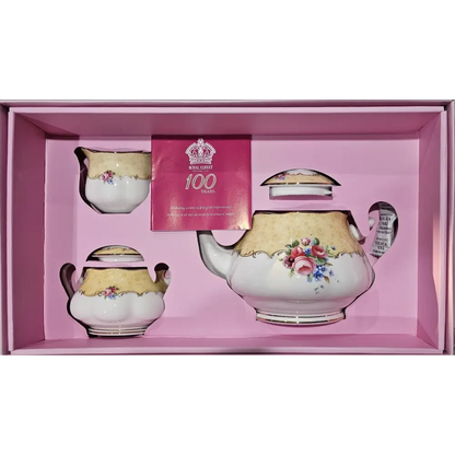 Tea set with floral designs in a pink box, featuring a card with a crown and text.