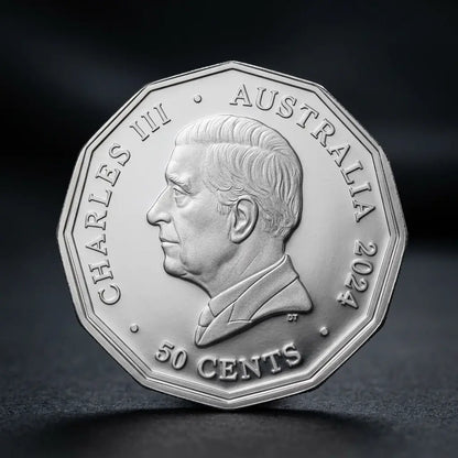 A silver Australian 50 cents coin featuring a profile portrait of Charles III, photographed on a dark, reflective surface.