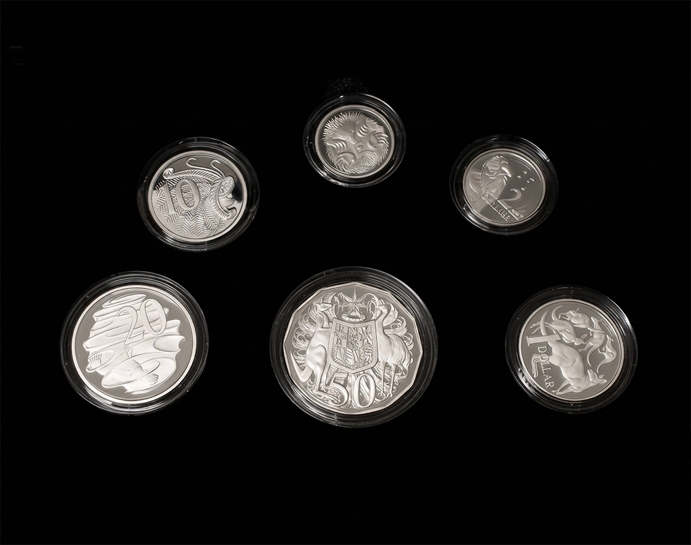 Five round silver coins in clear protective capsules, arranged on a solid black background. The coins feature various embossed designs including a lion, a crest, and other heraldic symbols from our Gold Proof Sets & Commemorative Medals collection