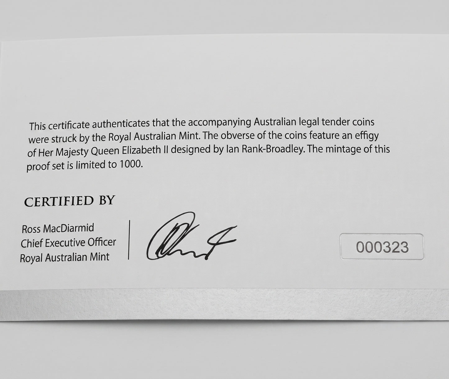 A close-up of a white certificate card from the Royal Australian Mint with printed text, a signature, and the number 000323.