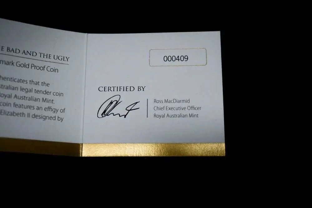 An open white coin certification booklet with gold foil at the bottom, showing printed text including 'Certified by' and a signature, photographed against a black background.