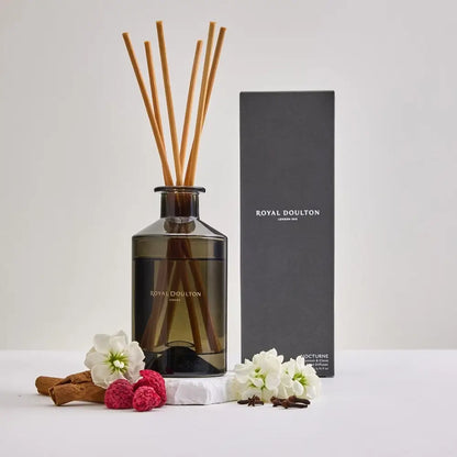 Royal Doulton diffuser with reeds, flowers, and cinnamon sticks on a white background