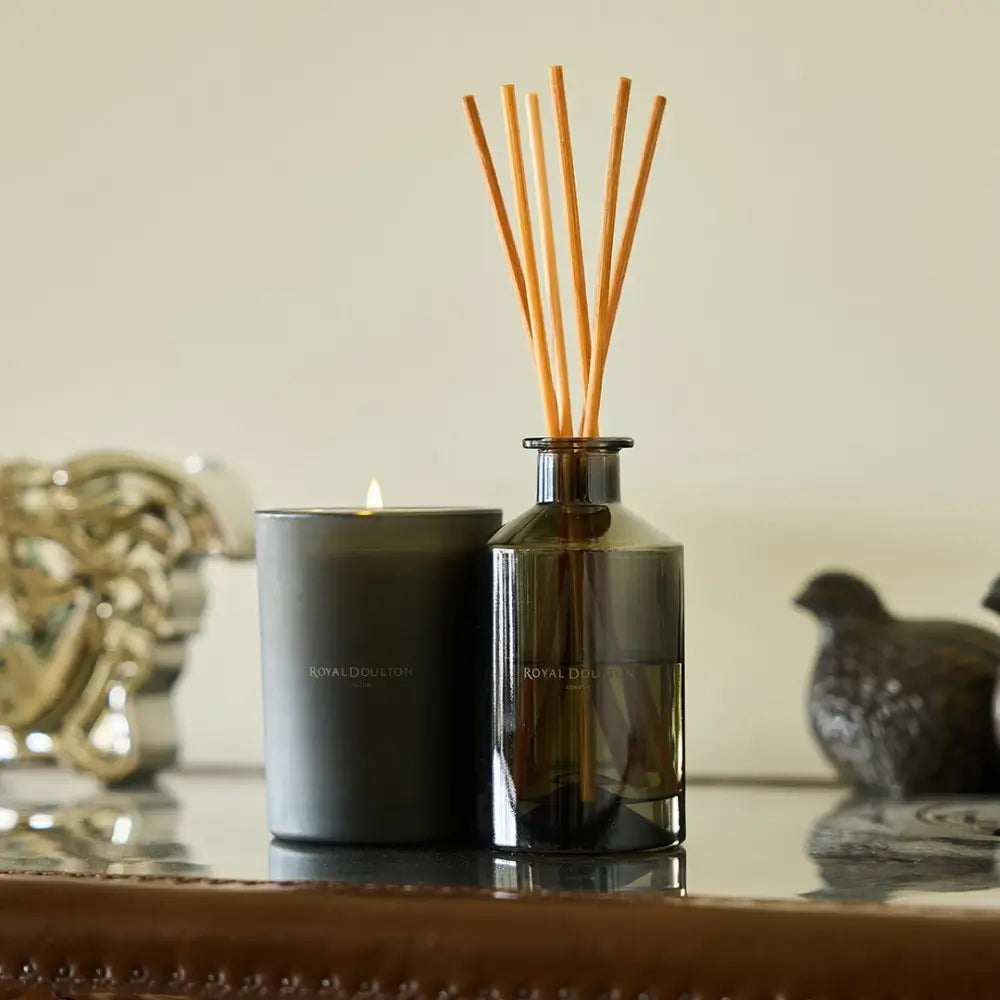 Candle and diffuser with wooden sticks on a reflective surface