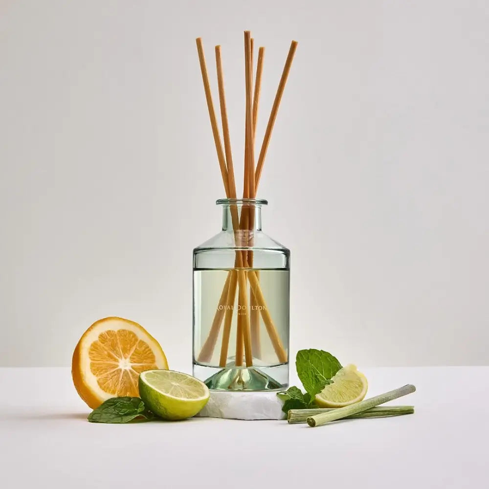 Reed diffuser with wooden sticks in a glass bottle surrounded by citrus fruits and mint leaves