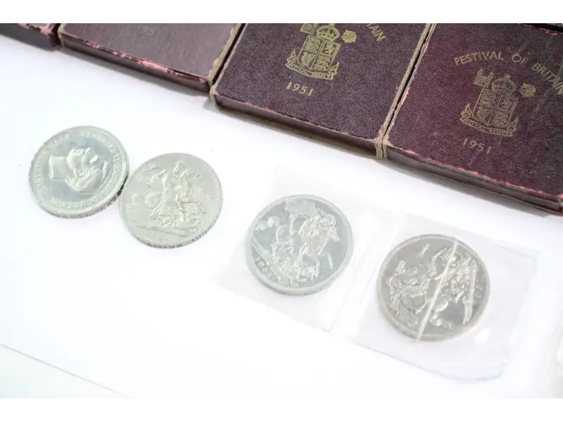 Four silver coins with a decorative design on a white surface, with a purple album in the background.