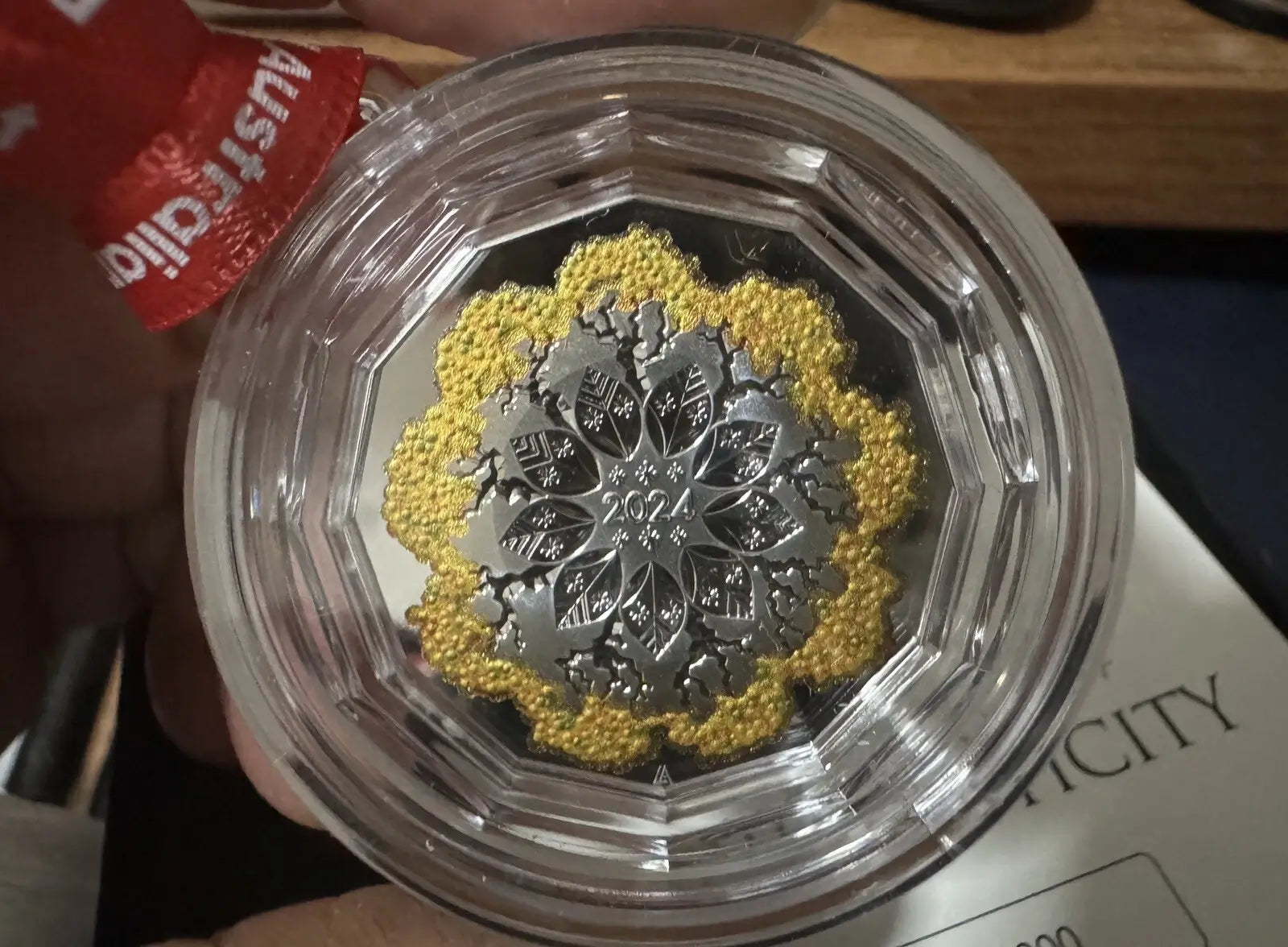 A close-up of a collectible Australian 2023 Gold and Silver Double Coin Medal inside a clear plastic protective capsule, held by a hand.