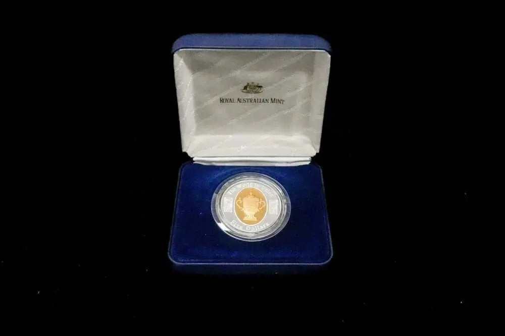 A collectible coin presented in an open blue velvet case against a black background. The coin is housed in a clear circular holder, with a gold-toned inner ring, and the case lid is lined with white satin featuring the text 'ROYAL AUSTRALIAN Mint'.