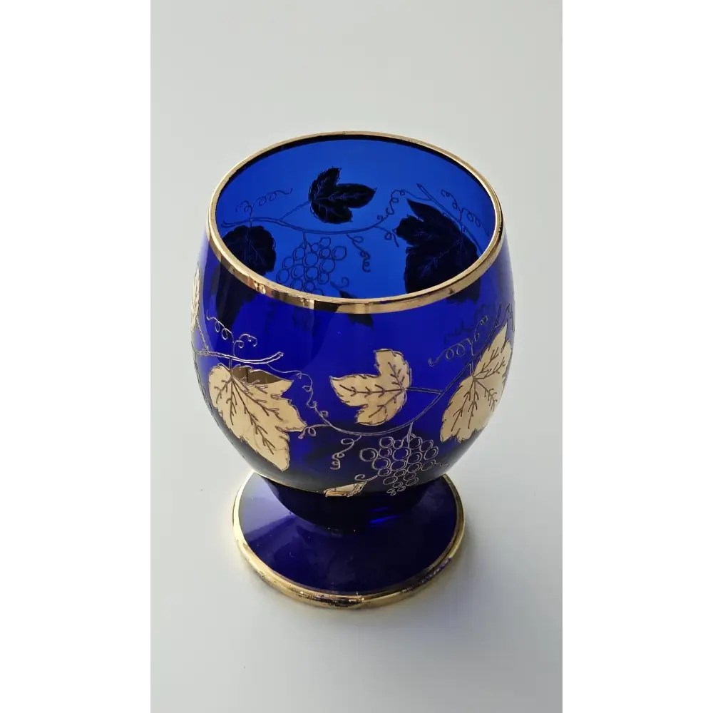 Blue glass goblet with gold leaf and vine patterns on a white background