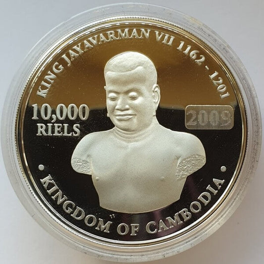 A round commemorative coin of Cambodia, featuring King Jayavarman VII, displayed inside a clear protective plastic capsule. The coin has a gold and black background with silver-toned relief details and text reading '10,000 RIELS' and '2009'.