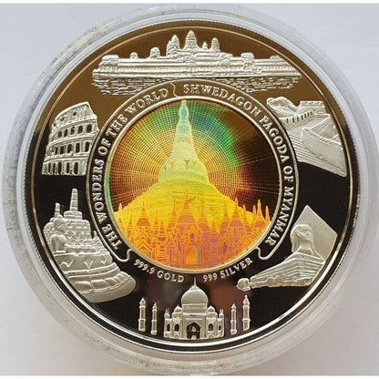 A round commemorative coin featuring a central golden pagoda with iridescent rainbow effects, surrounded by silhouettes of landmarks including the Colosseum, Taj Mahal, and Angkor Wat, with text reading 'THE WONDERS OF THE WORLD / SHEDWAGON PAGODA OF MYANMAR' and metal purity markings.