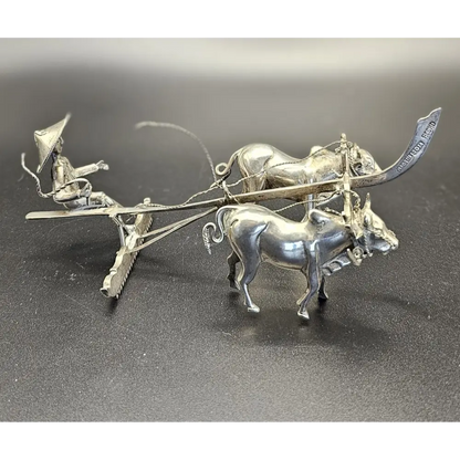 Silver sculpture of a farmer on a cart pulled by two oxen on a dark surface