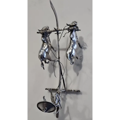 Metallic sculpture of three figures on a branch against a light gray background