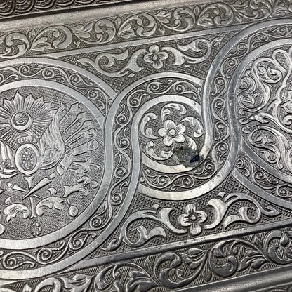 Close-up of intricate silver embossing with floral and geometric patterns.