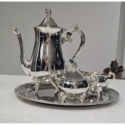 Silver tea set with teapot, sugar bowl, creamer, and tray on a white surface.