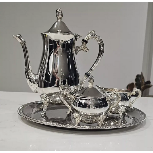 Silver tea set with teapot, sugar bowl, creamer, and tray on a white surface.