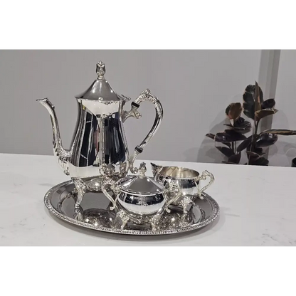 Silver tea set with teapot, creamer, sugar bowl, and tray on a white surface.