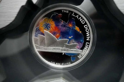 A round silver coin featuring the Sydney Opera House and colorful fireworks over an Australian map, displayed inside a clear protective case.