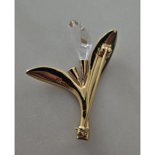 Gold leaf-shaped object with a crystal at the center on a gray background