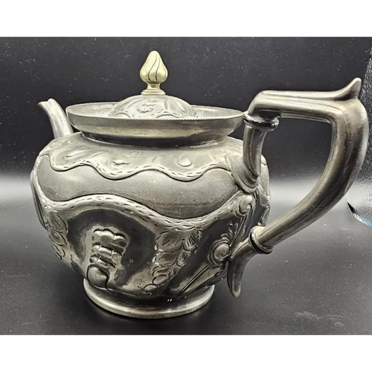 Decorative silver teapot with intricate designs on a black background