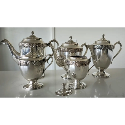 Silver tea set with ornate designs on a white surface