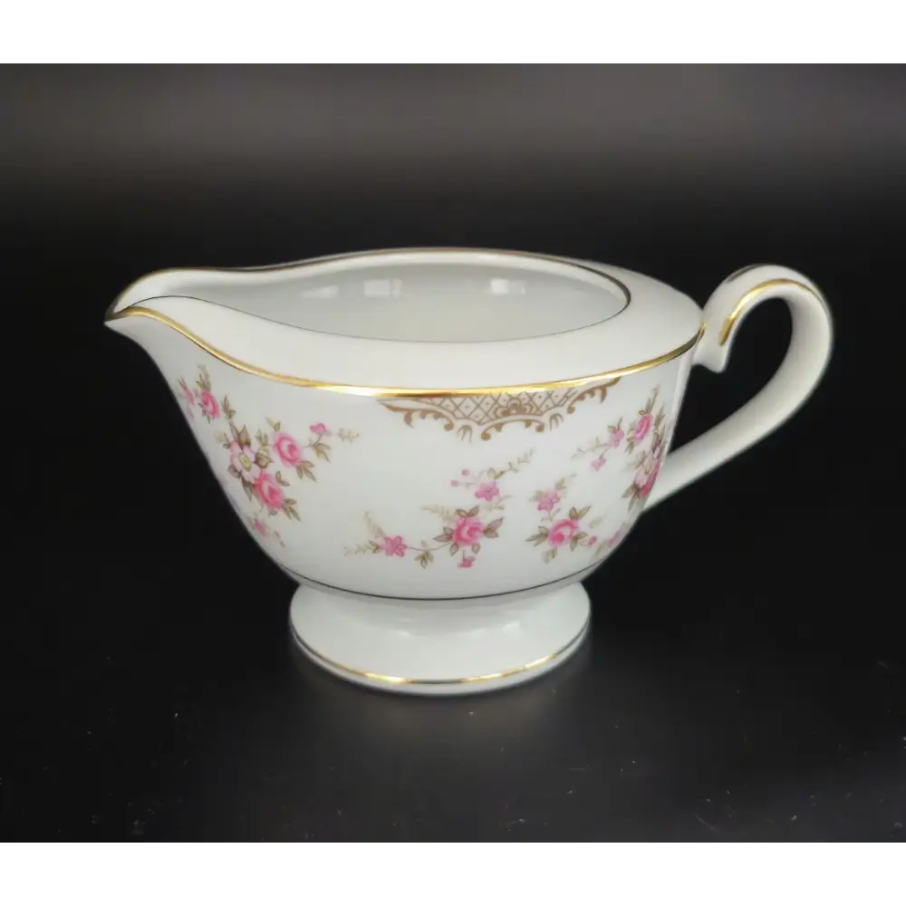 White ceramic creamer with floral design and gold accents