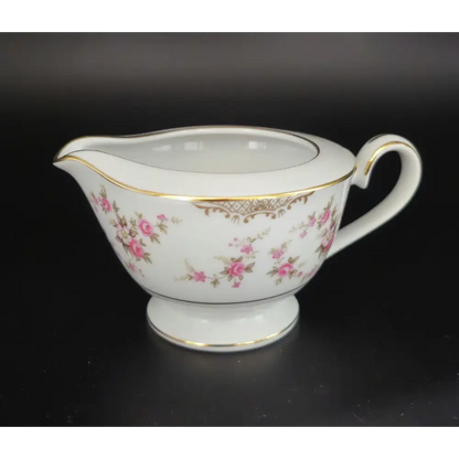 White ceramic creamer with floral design and gold accents