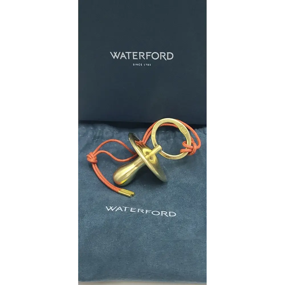 Gold pacifier with orange cord on a Waterford branded background