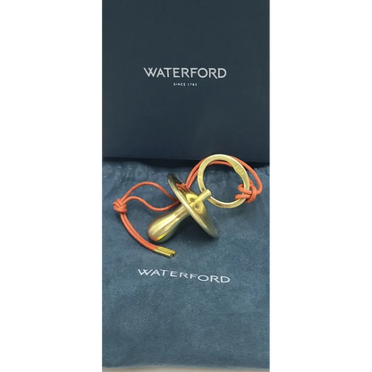 Gold pacifier with orange cord on a Waterford branded background
