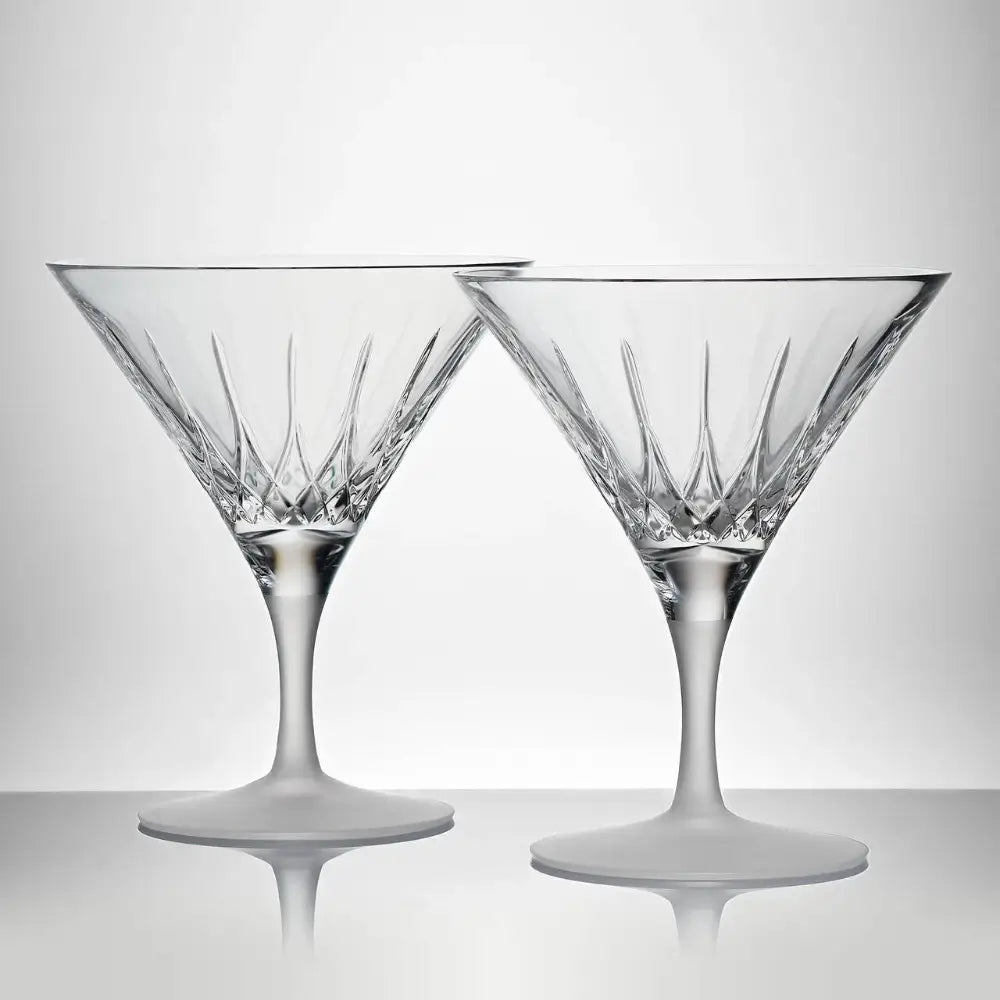 Two crystal martini glasses on a reflective surface with a light gray background