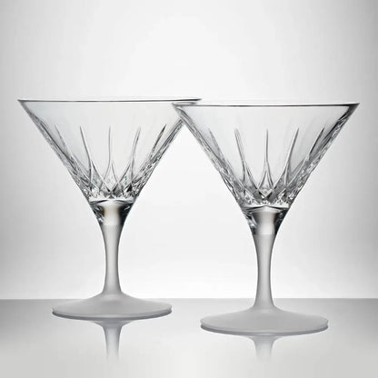 Two crystal martini glasses on a reflective surface with a light gray background