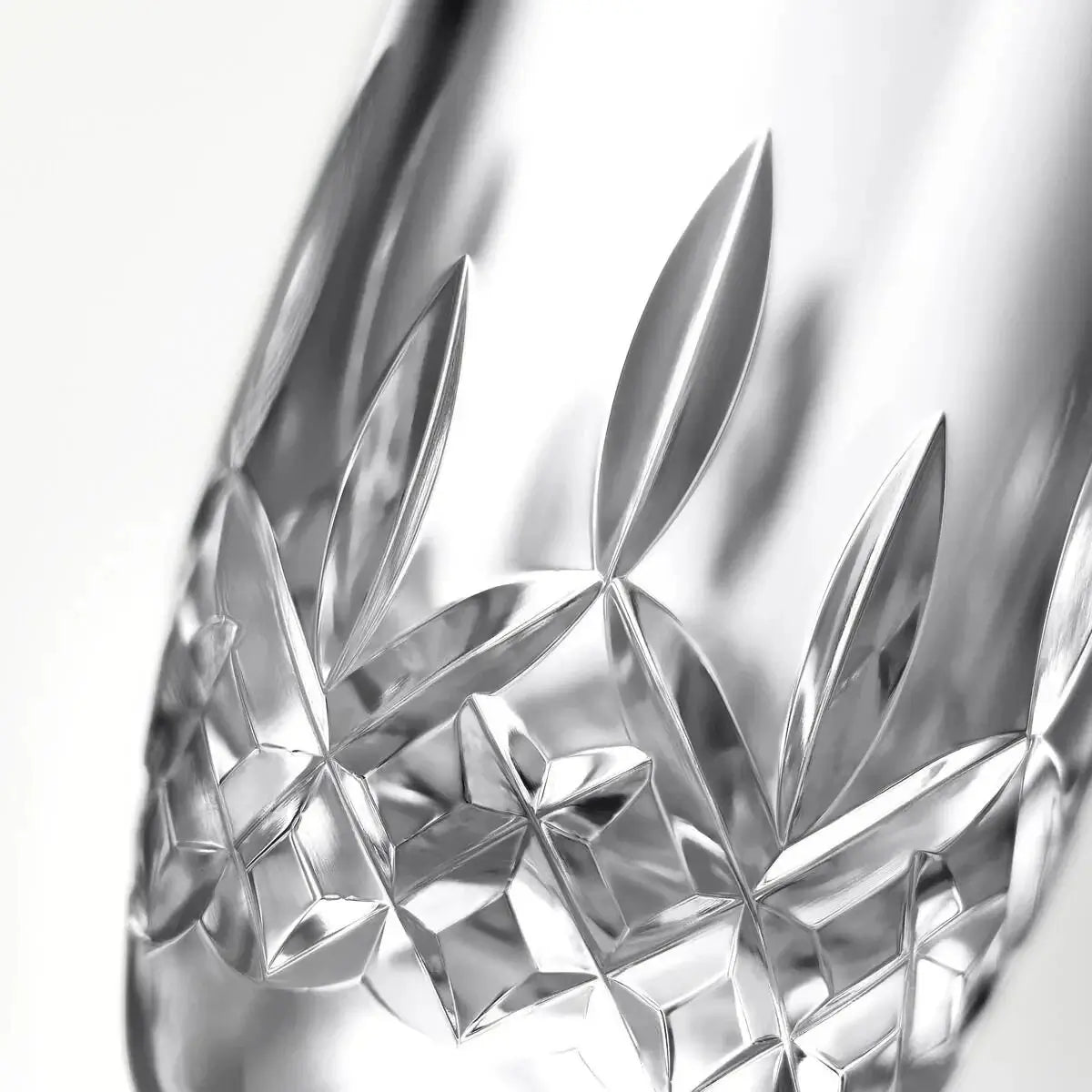 Close-up of a clear cut-glass or crystal object with reflective geometric and leaf-like facets on a white background.